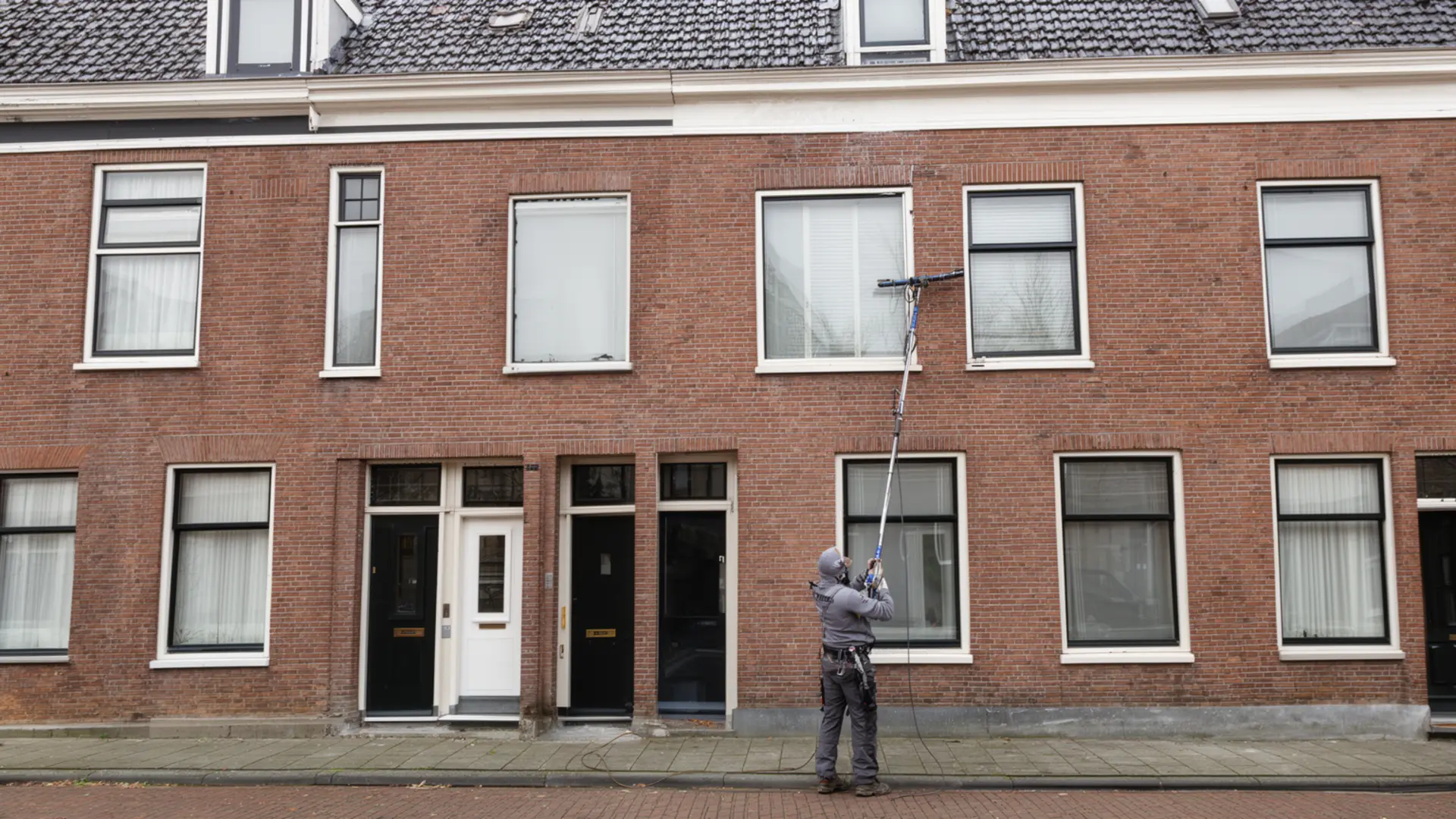 Glazenwasser wast de ramen van een rijtjeshuis met een telescoopsteel